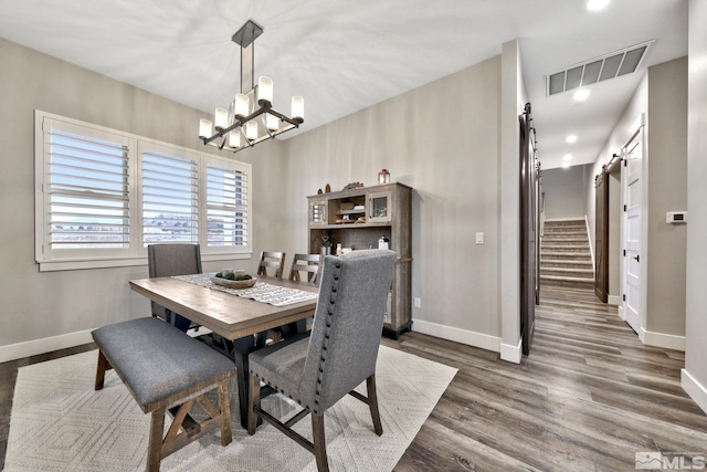 dining area with a barn door, a chandelier, and dark hardwood / wood-style flooring