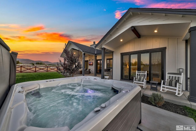 pool at dusk with a patio area and a hot tub