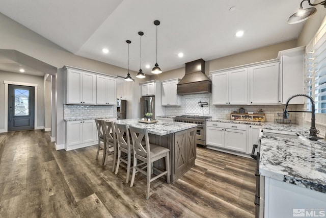 kitchen featuring a kitchen island, tasteful backsplash, white cabinets, custom exhaust hood, and appliances with stainless steel finishes