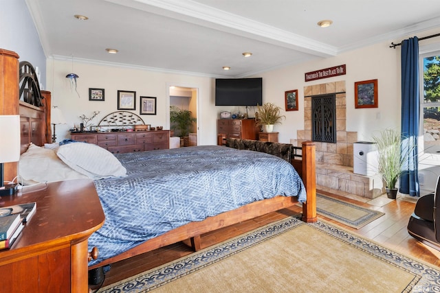 bedroom with a fireplace, wood-type flooring, crown molding, and beam ceiling