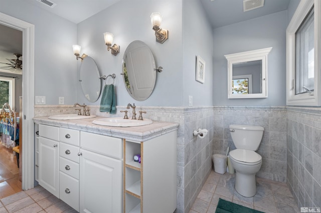 bathroom with tile patterned flooring, ceiling fan, toilet, tile walls, and vanity