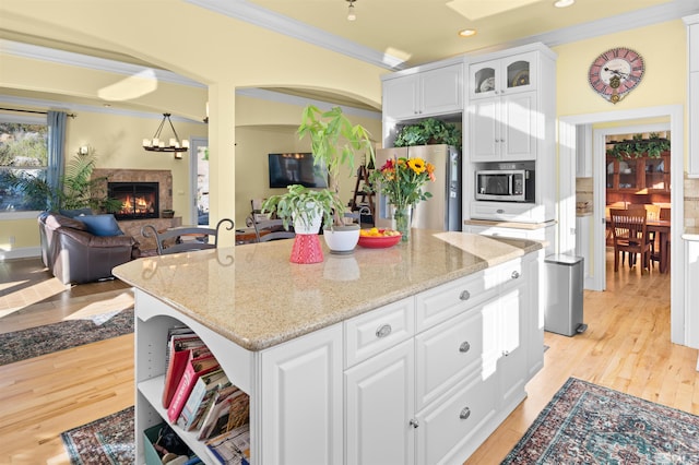 kitchen with white cabinets, ornamental molding, appliances with stainless steel finishes, a center island, and light hardwood / wood-style floors