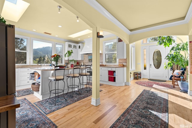 entryway featuring light hardwood / wood-style floors, crown molding, a skylight, and a healthy amount of sunlight