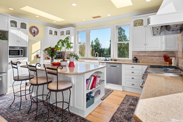 kitchen featuring stainless steel appliances, a kitchen island, exhaust hood, and white cabinetry