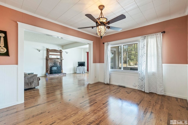 unfurnished living room with ornamental molding, a brick fireplace, ceiling fan, and wood-type flooring