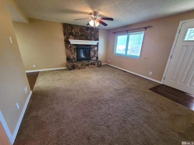 unfurnished living room with dark colored carpet, ceiling fan, a stone fireplace, and a textured ceiling