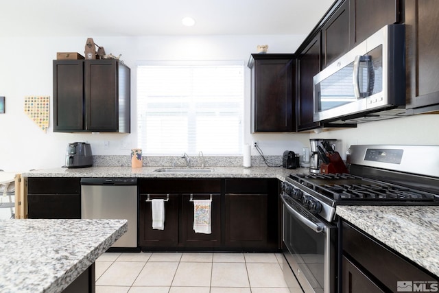 kitchen with dark brown cabinets, light stone counters, sink, stainless steel appliances, and light tile patterned floors