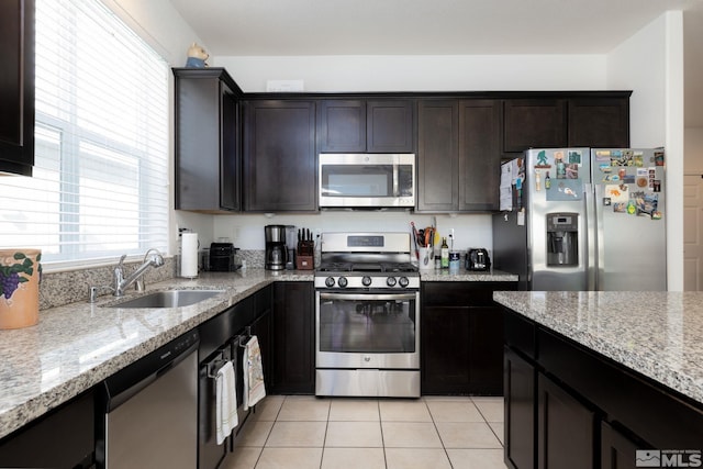 kitchen featuring stainless steel appliances, dark brown cabinetry, sink, and light stone counters