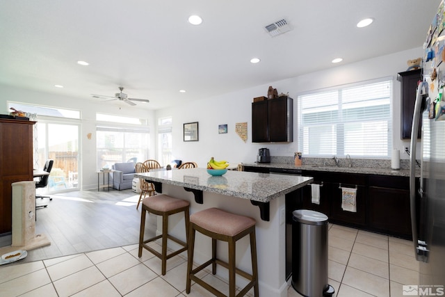 kitchen featuring light wood-type flooring, light stone counters, ceiling fan, a kitchen island, and a breakfast bar area