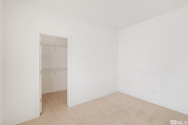 unfurnished bedroom featuring a closet, light colored carpet, and a walk in closet