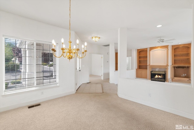 unfurnished dining area with ceiling fan with notable chandelier and light colored carpet