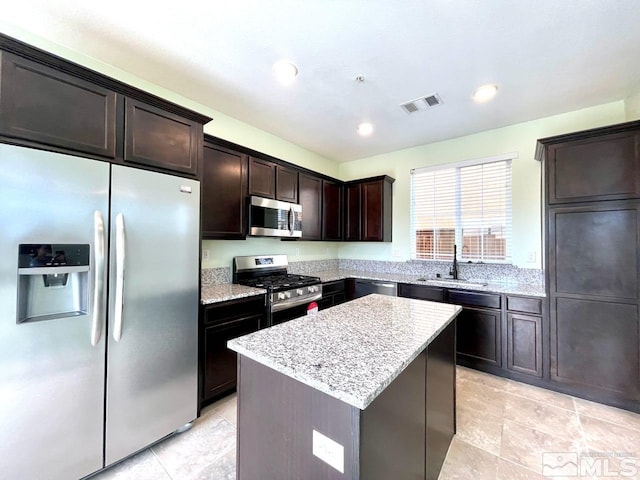 kitchen featuring dark brown cabinetry, sink, light stone counters, appliances with stainless steel finishes, and a center island