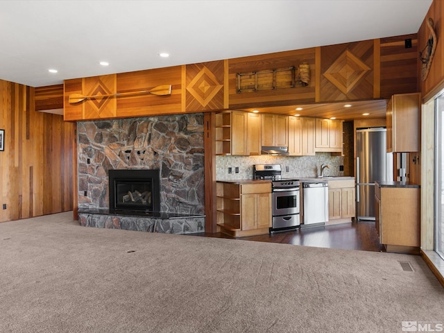 kitchen featuring wooden walls, a fireplace, dark carpet, appliances with stainless steel finishes, and backsplash