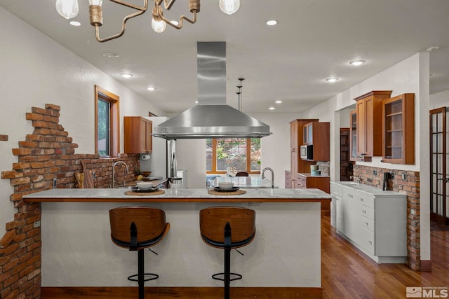 kitchen with kitchen peninsula, island exhaust hood, white cabinetry, a breakfast bar, and light hardwood / wood-style floors