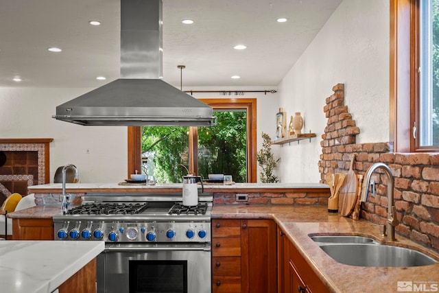 kitchen with light stone countertops, sink, high end range, island exhaust hood, and decorative light fixtures