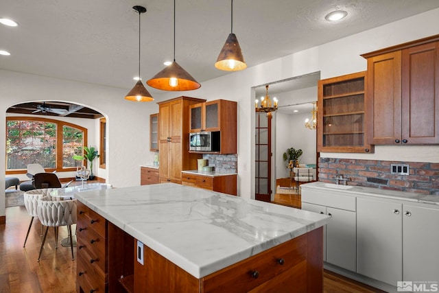 kitchen featuring decorative light fixtures, dark wood-type flooring, light stone countertops, stainless steel microwave, and decorative backsplash