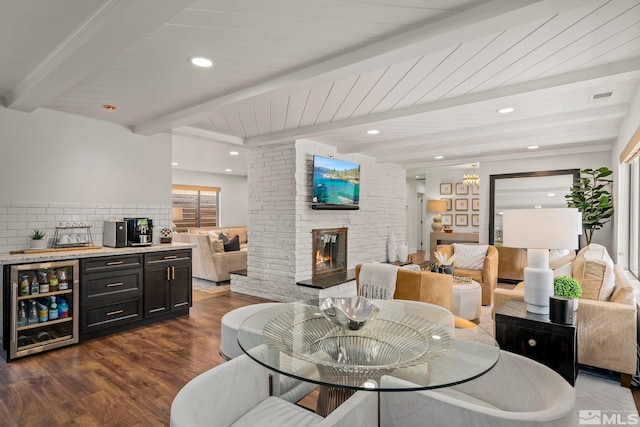 dining area featuring beamed ceiling, bar area, beverage cooler, dark hardwood / wood-style flooring, and a large fireplace