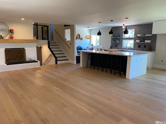 kitchen featuring light wood-type flooring, a breakfast bar area, decorative light fixtures, a spacious island, and white cabinetry