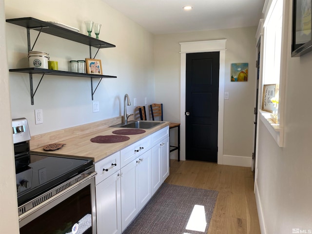 kitchen featuring stainless steel electric stove, white cabinets, wooden counters, sink, and light hardwood / wood-style floors