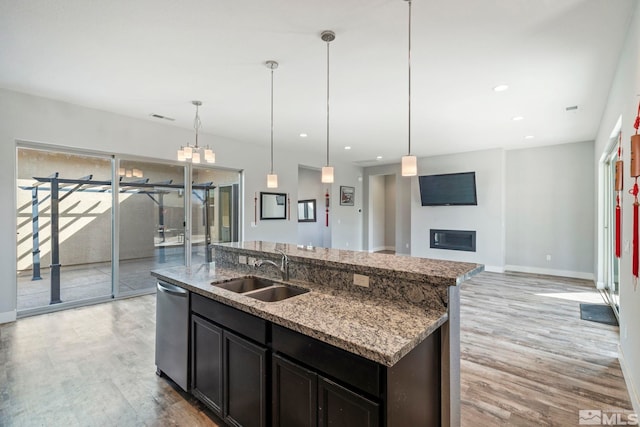 kitchen with hanging light fixtures, light hardwood / wood-style floors, a kitchen island with sink, and sink