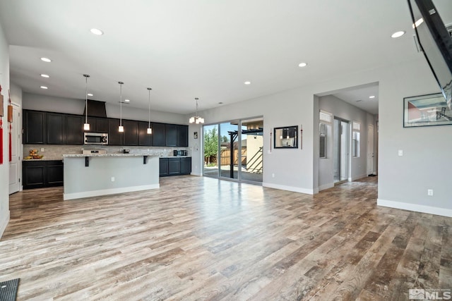 kitchen with light wood-type flooring, pendant lighting, a kitchen island, light stone counters, and a kitchen bar