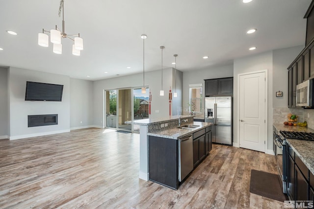 kitchen with sink, decorative light fixtures, a kitchen island with sink, stainless steel appliances, and light wood-type flooring