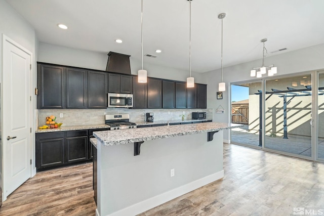 kitchen featuring pendant lighting, stainless steel appliances, a center island, light wood-type flooring, and a kitchen bar