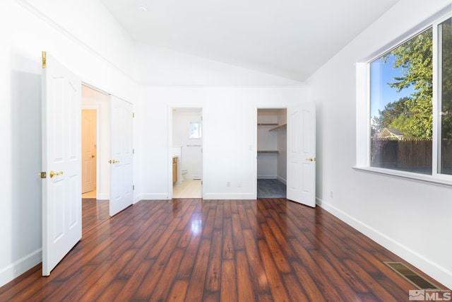 unfurnished bedroom featuring lofted ceiling, multiple windows, connected bathroom, and dark hardwood / wood-style floors