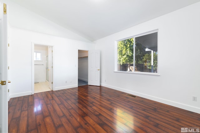 unfurnished bedroom with ensuite bath, vaulted ceiling, dark hardwood / wood-style floors, and a walk in closet