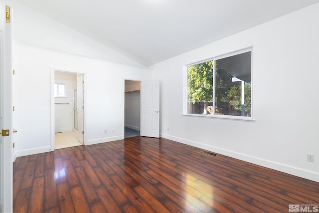 unfurnished bedroom featuring baseboards, a spacious closet, lofted ceiling, and hardwood / wood-style flooring