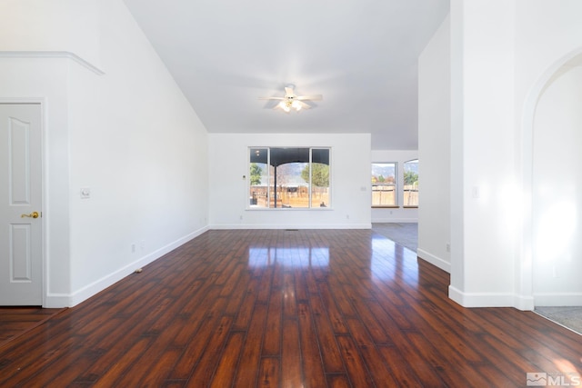 unfurnished living room featuring baseboards, arched walkways, a ceiling fan, dark wood finished floors, and vaulted ceiling