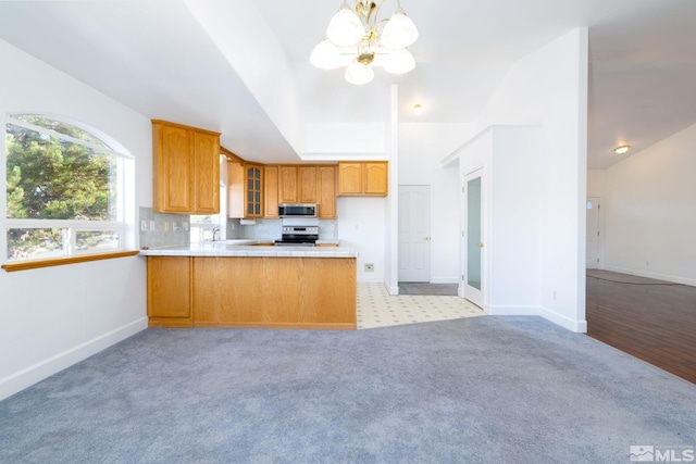 kitchen with tasteful backsplash, decorative light fixtures, lofted ceiling, kitchen peninsula, and appliances with stainless steel finishes