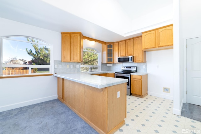 kitchen featuring baseboards, a peninsula, glass insert cabinets, decorative backsplash, and stainless steel appliances