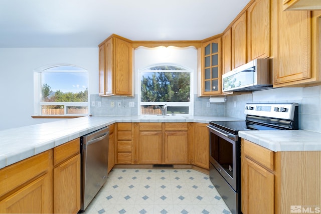 kitchen featuring appliances with stainless steel finishes, a healthy amount of sunlight, tile countertops, and backsplash