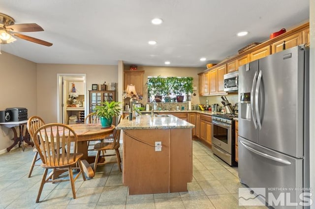 kitchen with kitchen peninsula, light stone counters, ceiling fan, light tile patterned flooring, and stainless steel appliances