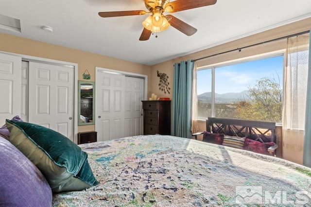 bedroom featuring ceiling fan, a mountain view, and two closets