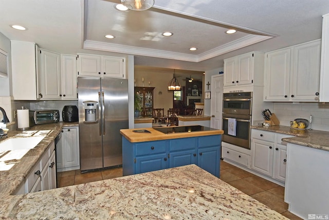 kitchen featuring decorative backsplash, a tray ceiling, blue cabinetry, stainless steel appliances, and white cabinetry