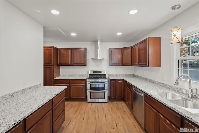 kitchen with stainless steel appliances, wall chimney exhaust hood, sink, light hardwood / wood-style floors, and decorative light fixtures