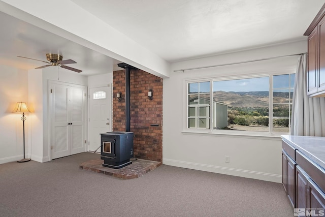 living room featuring a wood stove, light carpet, a mountain view, and ceiling fan