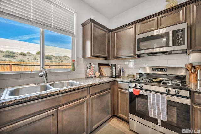 kitchen with dark brown cabinetry, sink, stone countertops, appliances with stainless steel finishes, and decorative backsplash