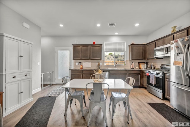 kitchen featuring appliances with stainless steel finishes, light wood-type flooring, dark brown cabinetry, and tasteful backsplash