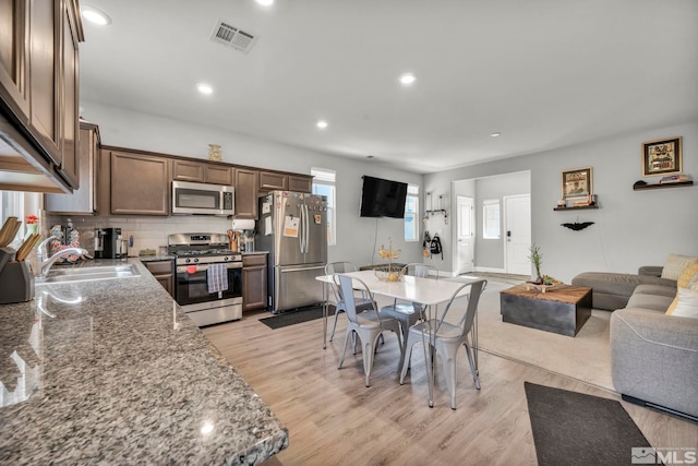 kitchen with light hardwood / wood-style floors, stone countertops, sink, decorative backsplash, and appliances with stainless steel finishes