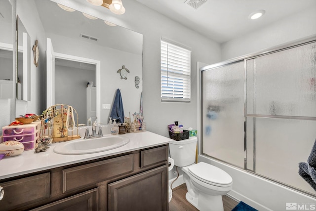 full bathroom featuring wood-type flooring, bath / shower combo with glass door, vanity, and toilet