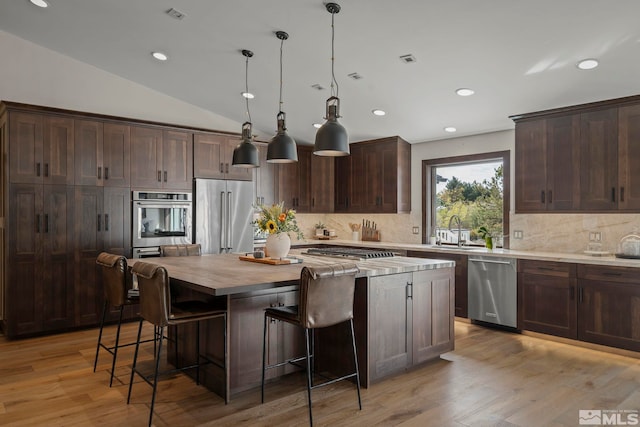 kitchen featuring pendant lighting, a kitchen island, light hardwood / wood-style flooring, stainless steel appliances, and lofted ceiling