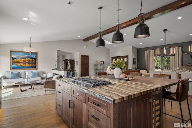 kitchen with vaulted ceiling with beams, hanging light fixtures, stainless steel gas stovetop, a center island, and light wood-type flooring