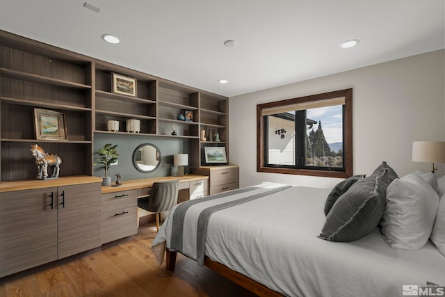 bedroom with built in desk and hardwood / wood-style floors