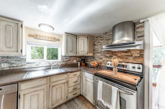 kitchen featuring appliances with stainless steel finishes, cream cabinetry, tasteful backsplash, and wall chimney range hood