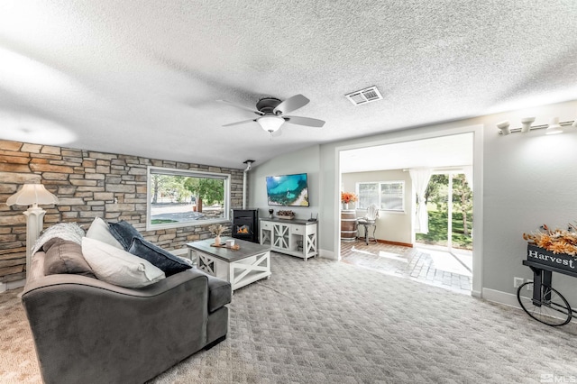 carpeted living room with ceiling fan, a textured ceiling, and a wood stove