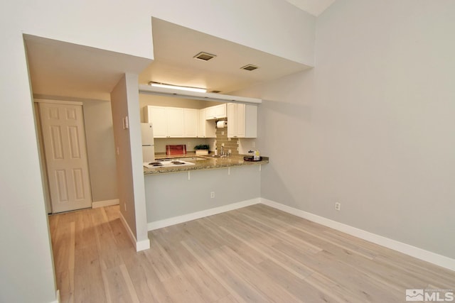 kitchen with kitchen peninsula, white fridge, white cabinetry, light stone countertops, and light hardwood / wood-style floors