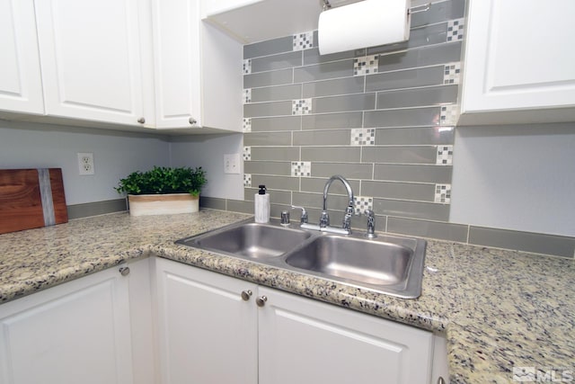 kitchen featuring backsplash, white cabinets, sink, and light stone counters